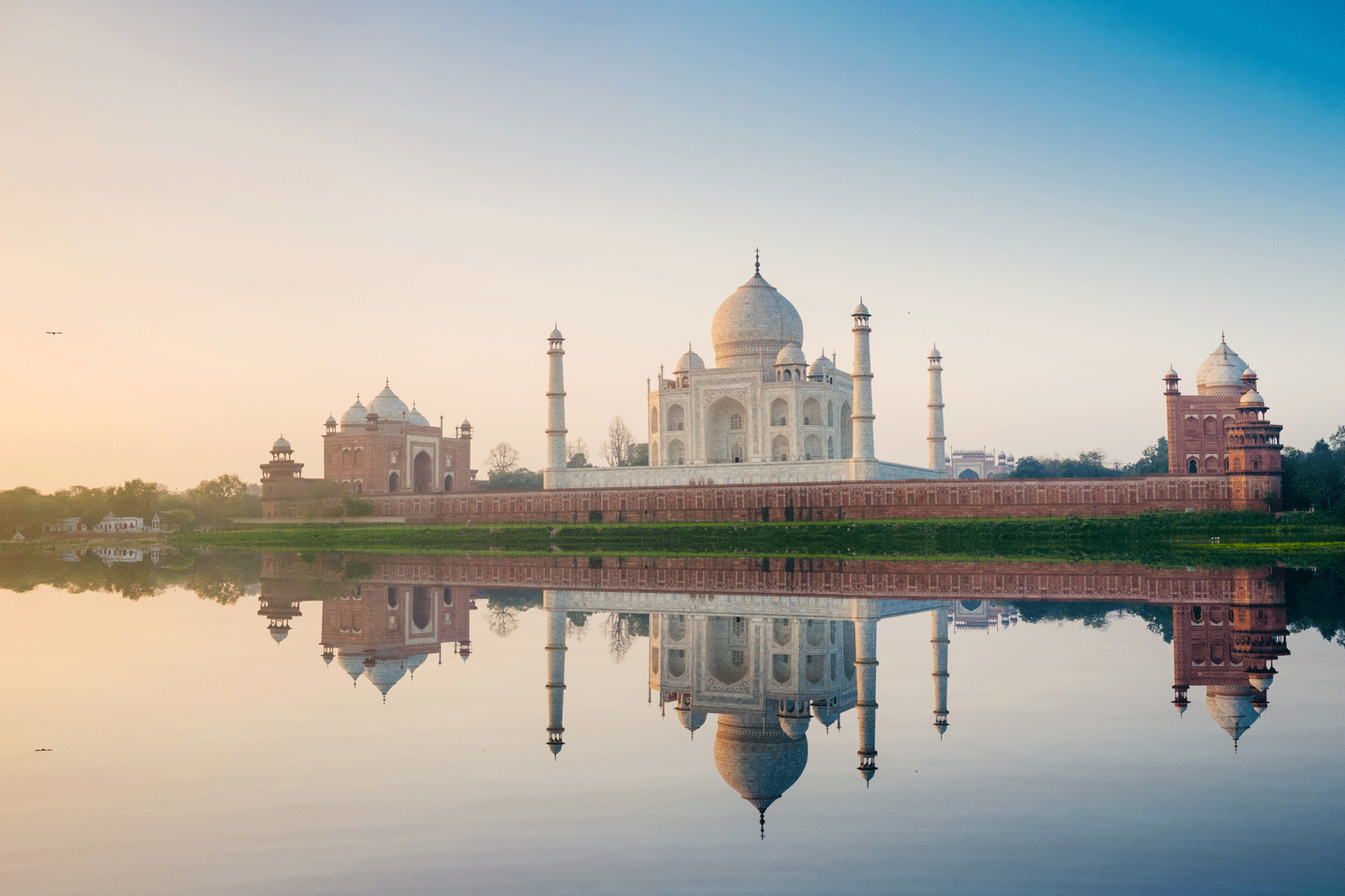 The taj mahal is reflected in the water.