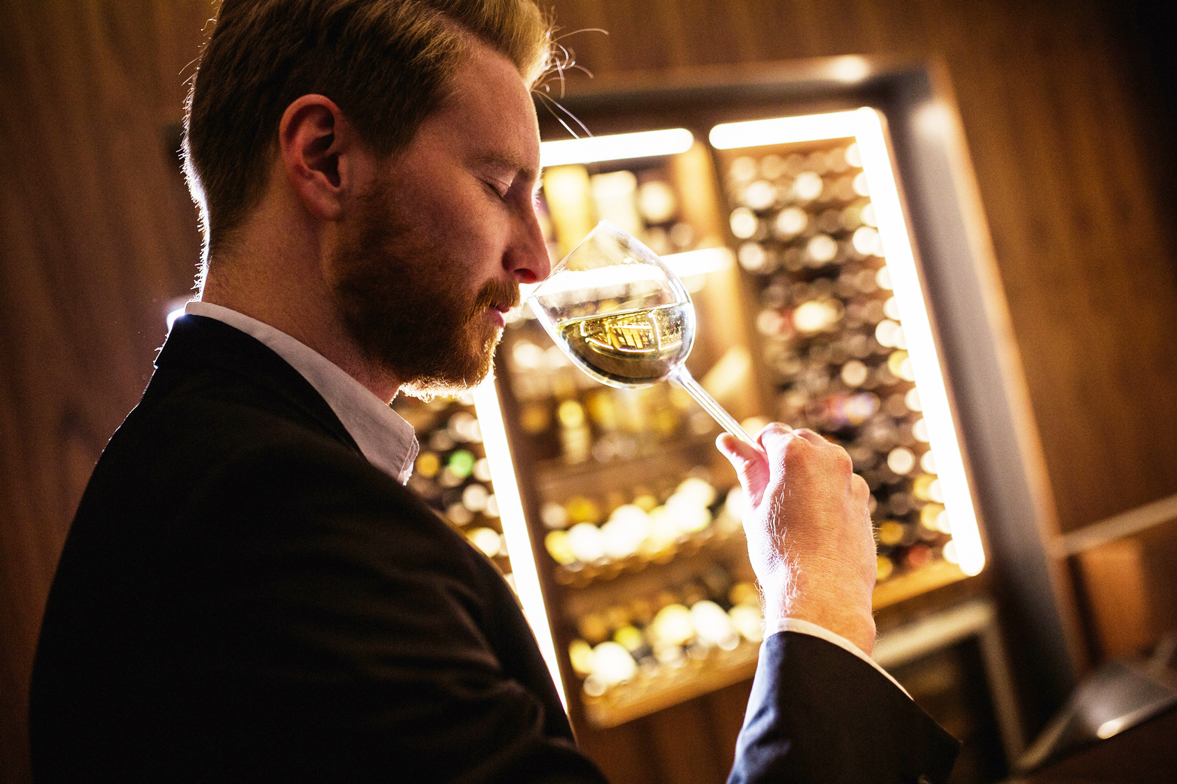 A man holding a German wine glass in front of a wine rack.