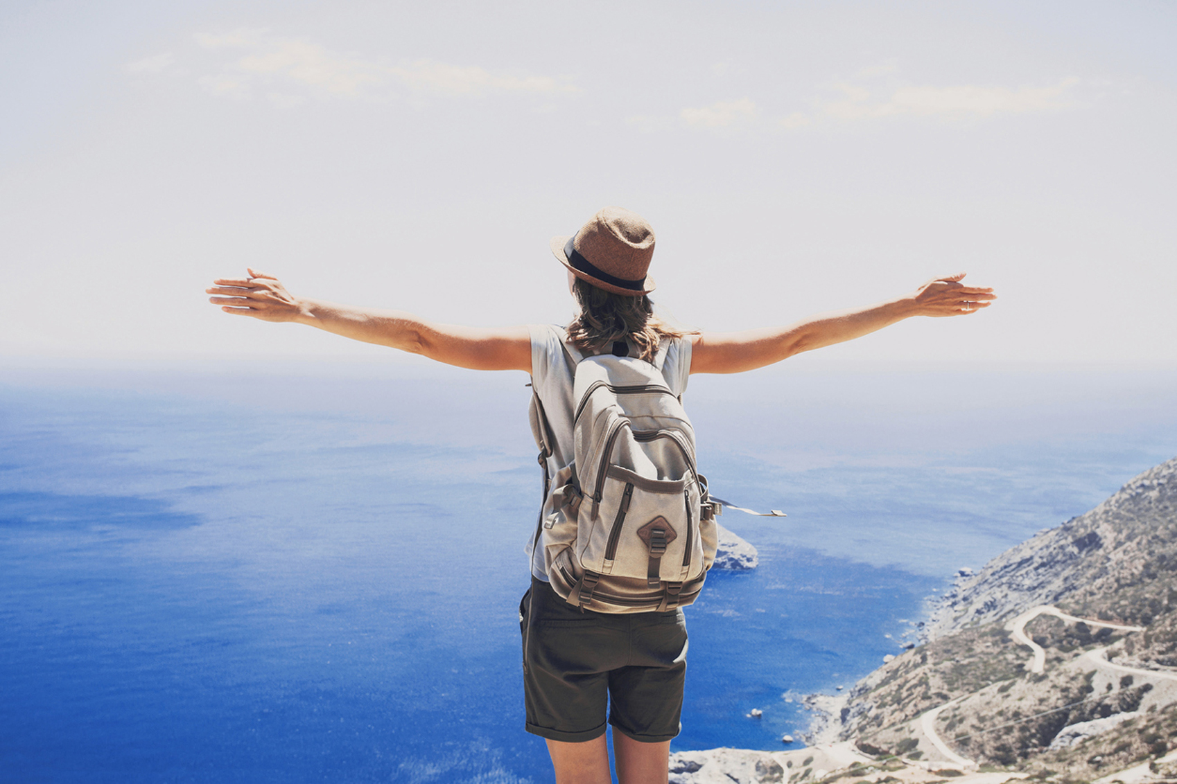 A woman experiencing the Benefits Of Solo Travel, with her arms outstretched on a cliff overlooking the ocean.