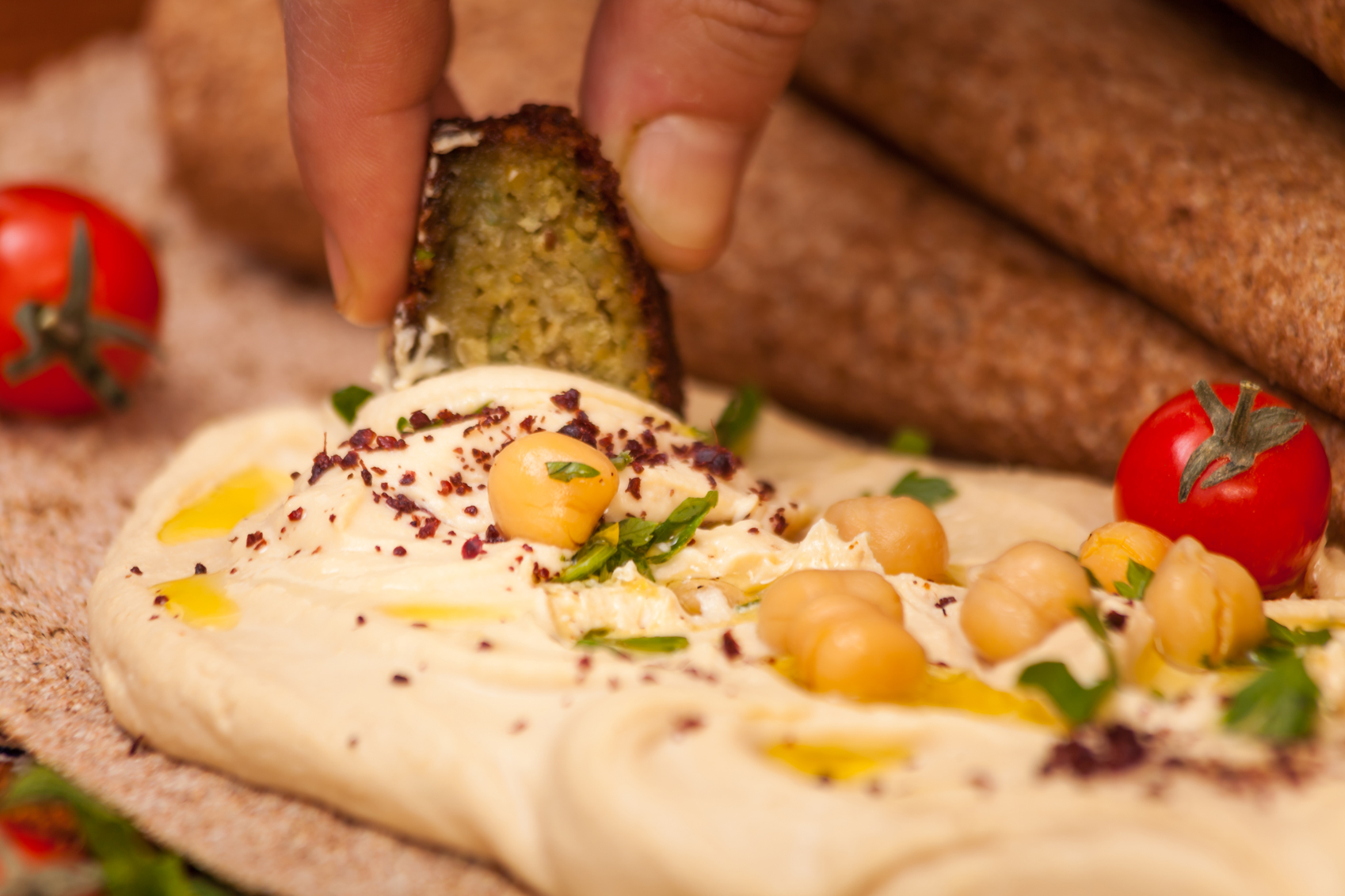 Fingers dipping gherkin into hummus