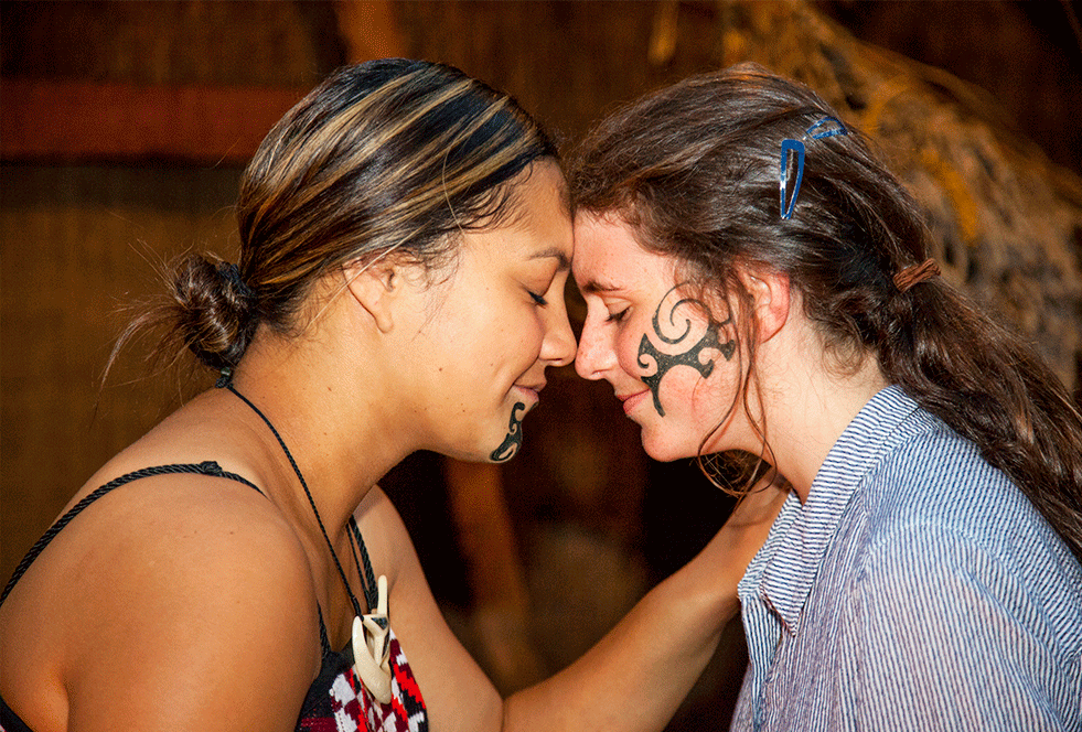 Two women embracing each other with Maori tribal tattoos on their faces.