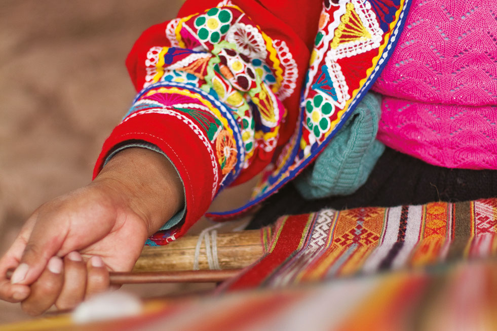 A Peruvian woman is weaving a colorful cloth on a loom.