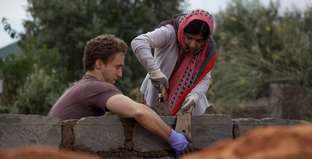 Two people working together to build a wall.