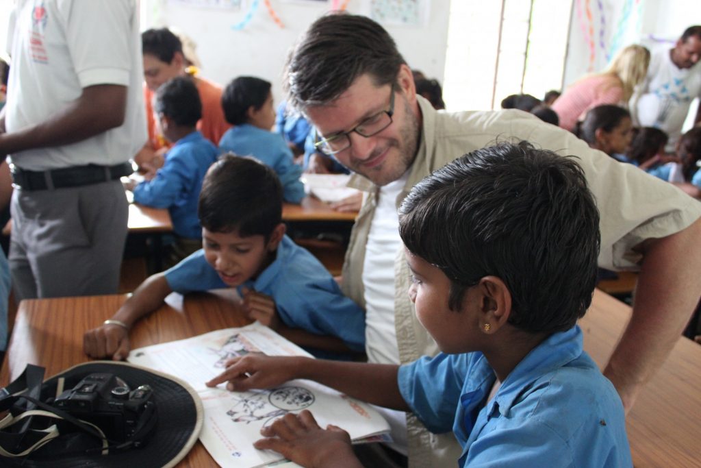A man in glasses is working with children in a classroom.