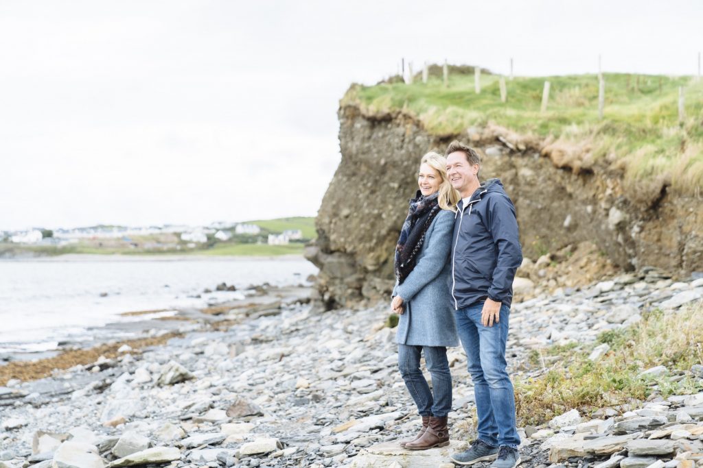 A couple standing on a rocky beach near the ocean.