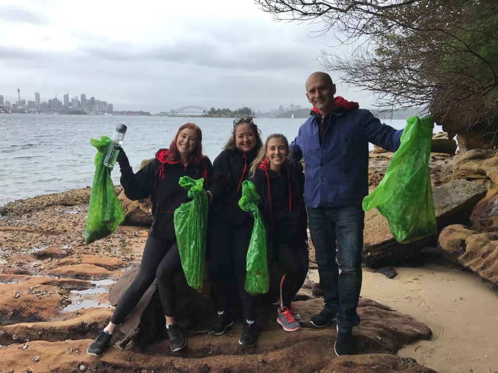 A group of people standing on a rocky beach with green bags.