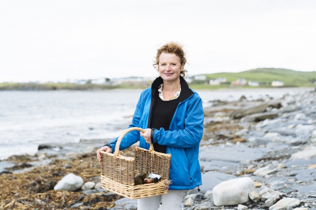 A woman holding a basket on a rocky beach.