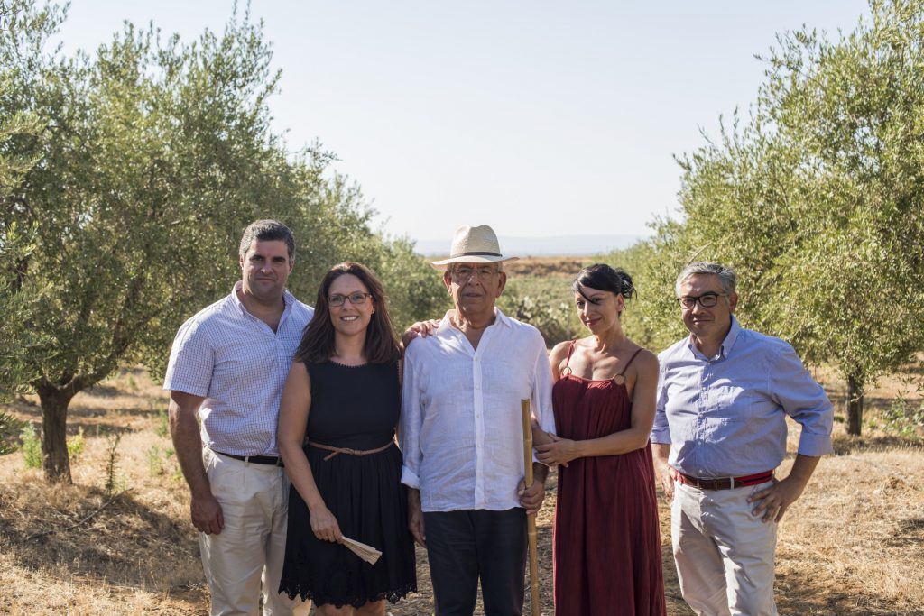 A group of people posing for a picture in an olive orchard.