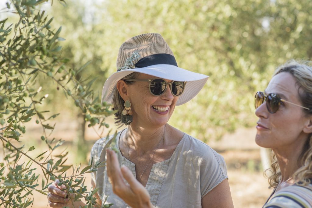 Two women in hats standing next to an olive tree.