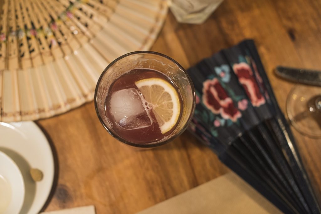 A drink with a lemon slice and a fan on a table.