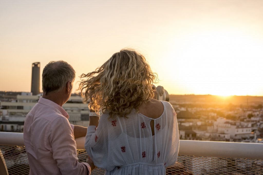 A couple looking at the sunset from a rooftop overlooking a city.