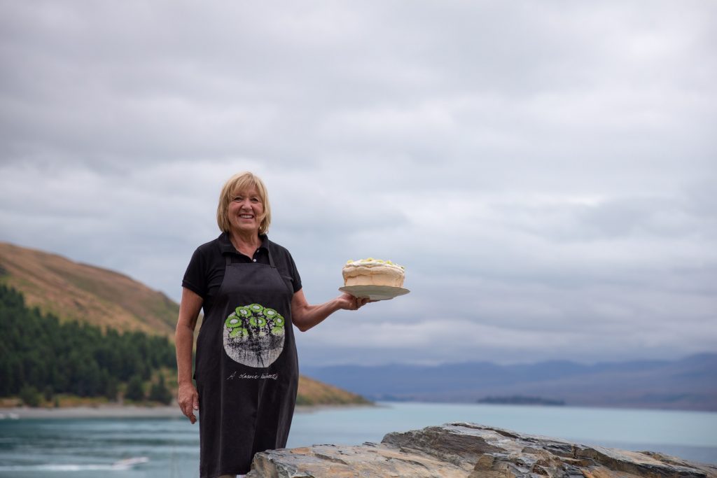 A woman holding a cake in front of a lake.