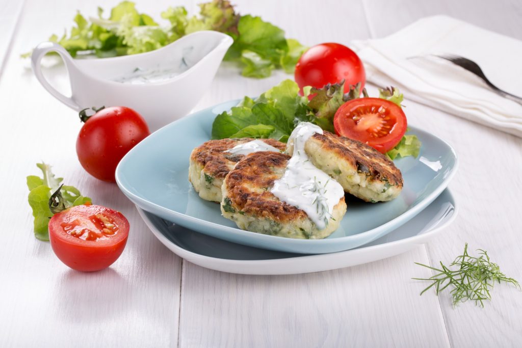 A plate with fish cakes, tomatoes and sour cream.