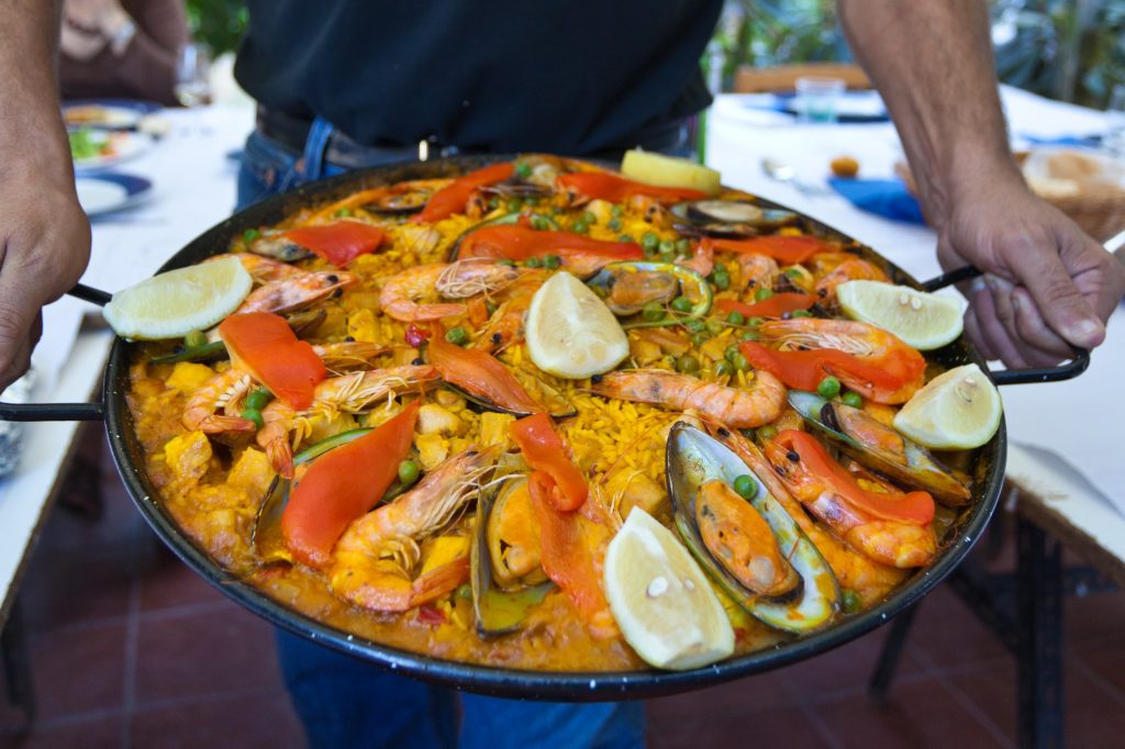 A man is holding a large pan of paella.