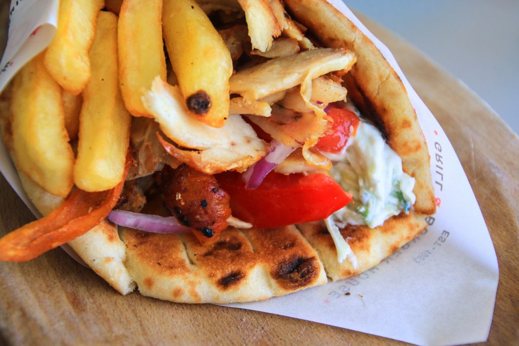 Indulge in a gyro sandwich infused with Greek flavors, served with fries on a wooden plate.