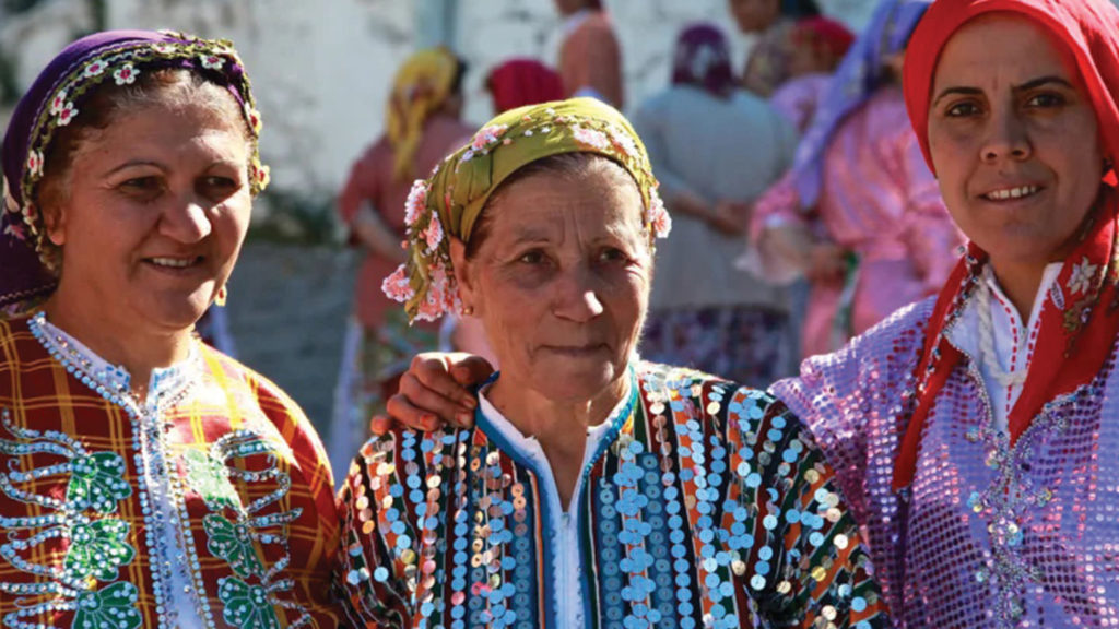 Three women dressed in colorful clothing are posing for a photo, showcasing Turkish customs.