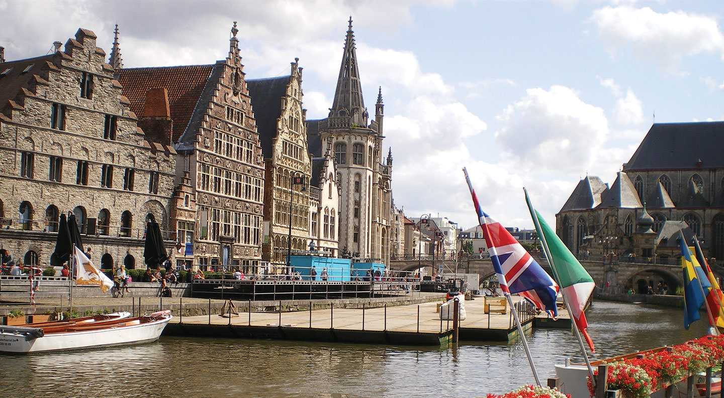 One of the Belgium attractions is a boat docked in a canal next to a row of buildings.
