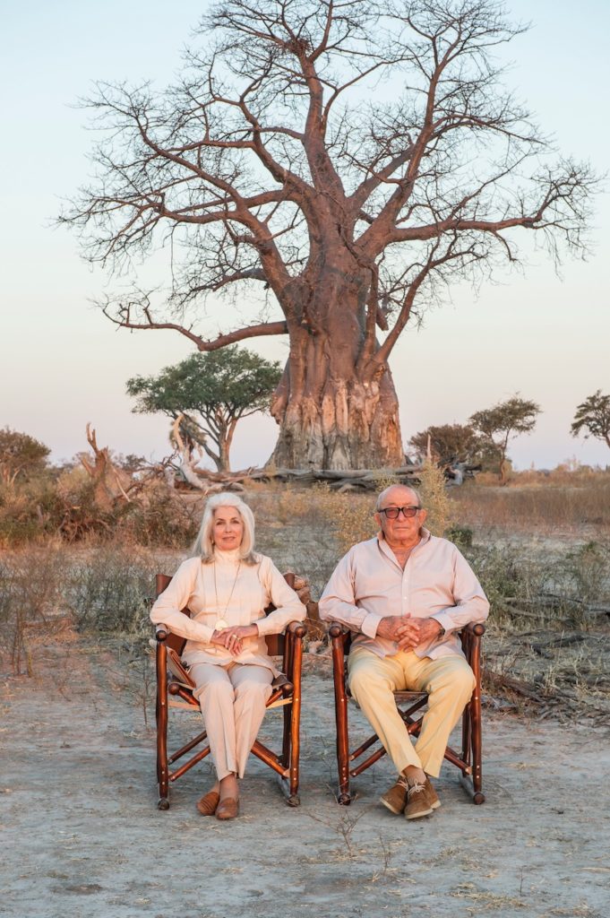 On Valentine's Day, two elderly people sit in chairs in front of a majestic baobab tree.