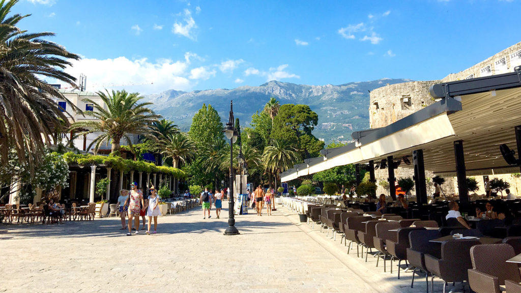 A street with tables and chairs in front of a mountain in Budva, Montenegro.