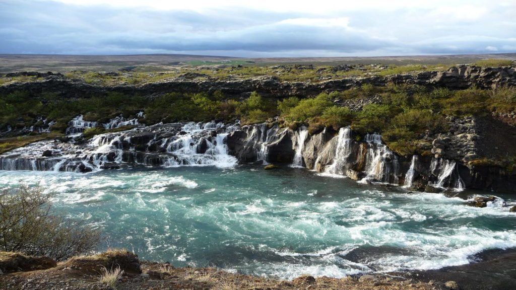 A waterfall in Iceland on my travel bucket list with a cloudy sky.