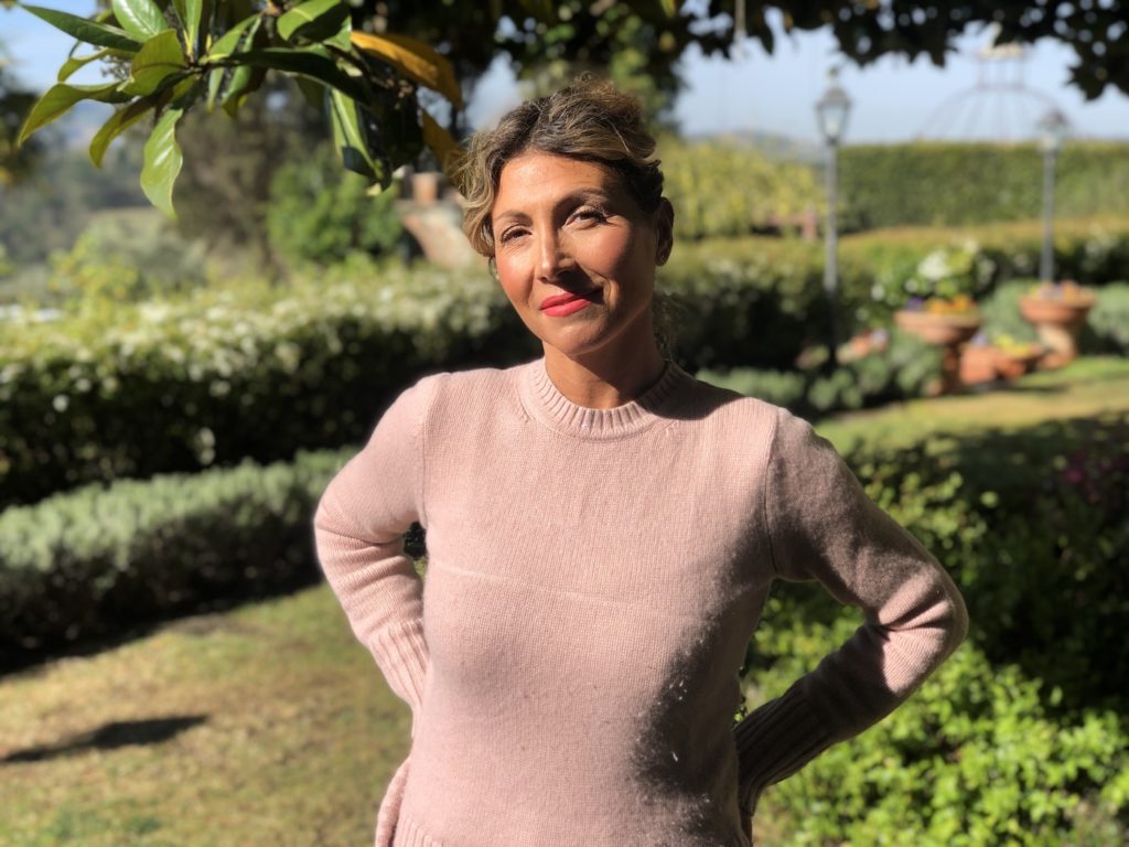 A woman in a pink sweater standing in a lush garden.