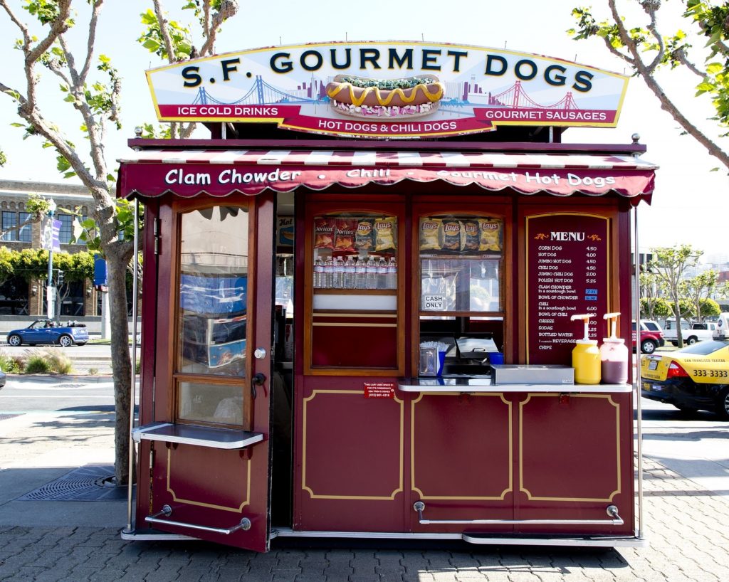 A red and white dog food stand sits on a busy California sidewalk.