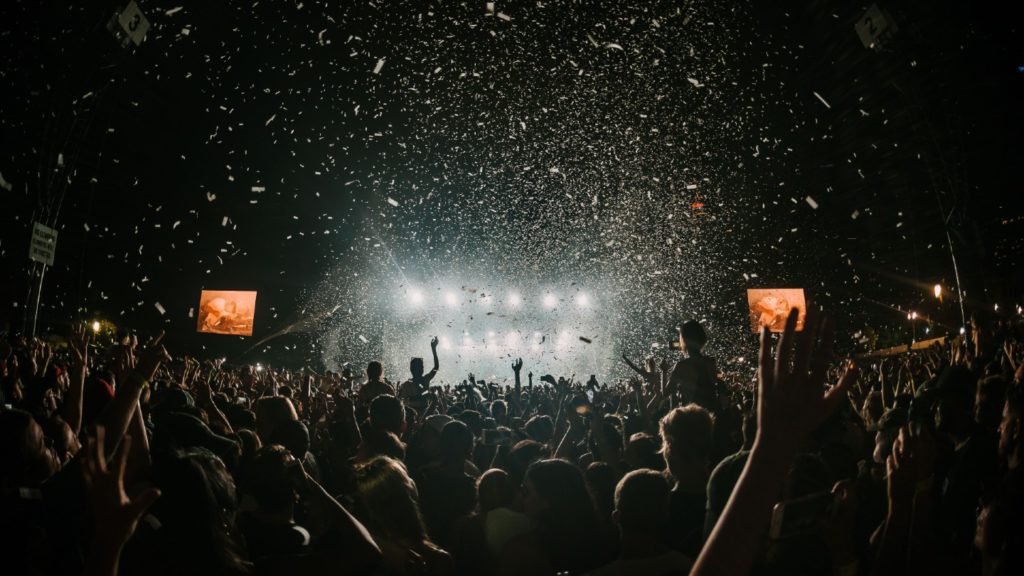 A crowd of concertgoers enjoying a live music performance at night with confetti falling from above, showcasing one reason why Aussies love Australia.