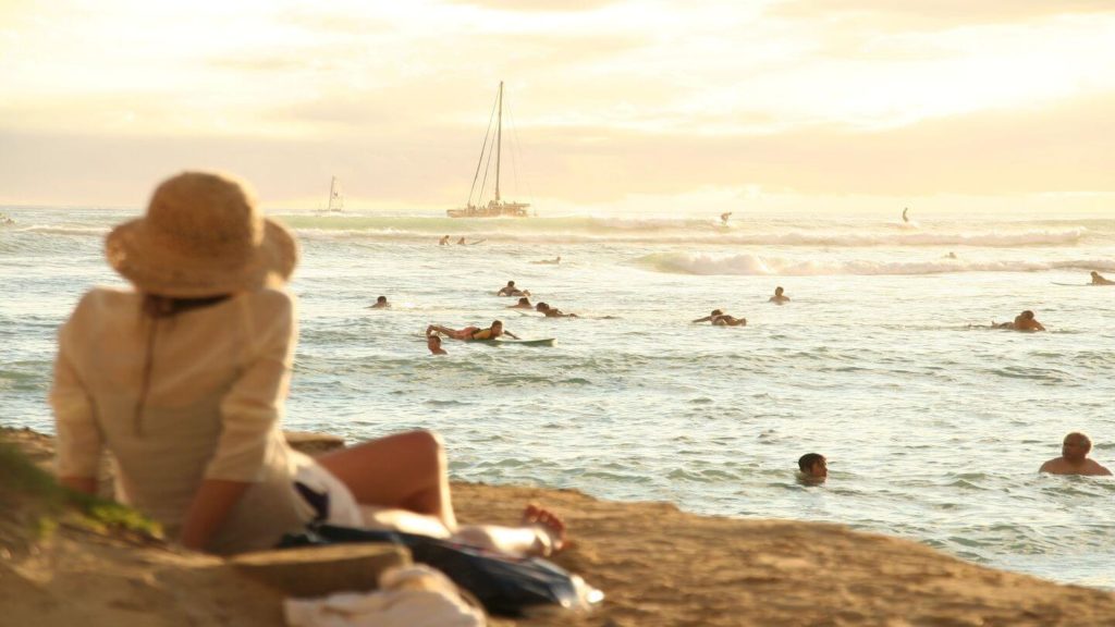 adult sitting on beach people swimming at sunset Hawaii