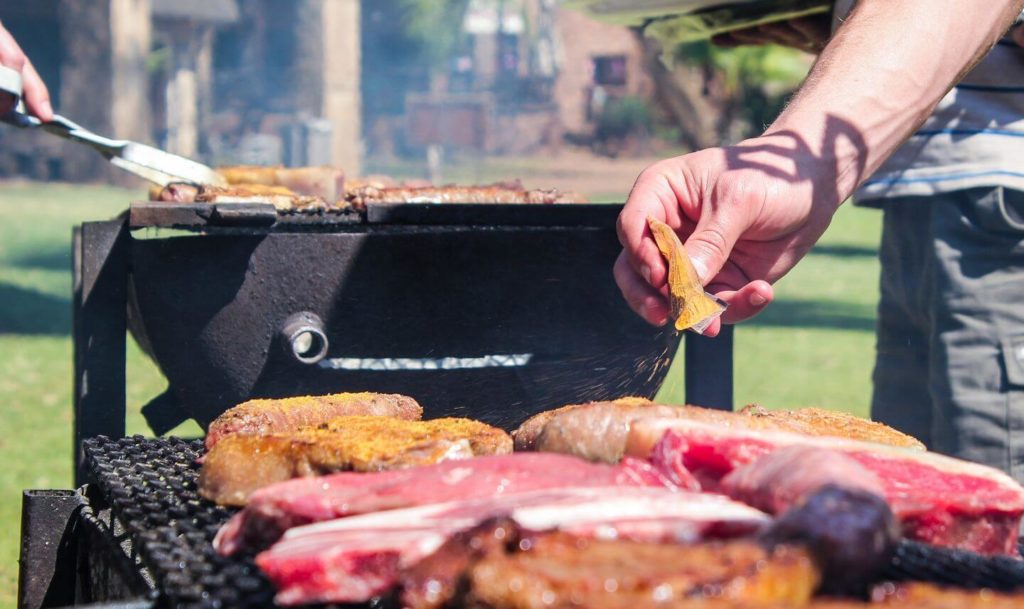 adult seasoning meat on a grill South African braai