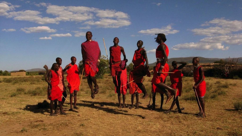 A group of people from the Maasai tribe standing in a field, wearing traditional red clothing.