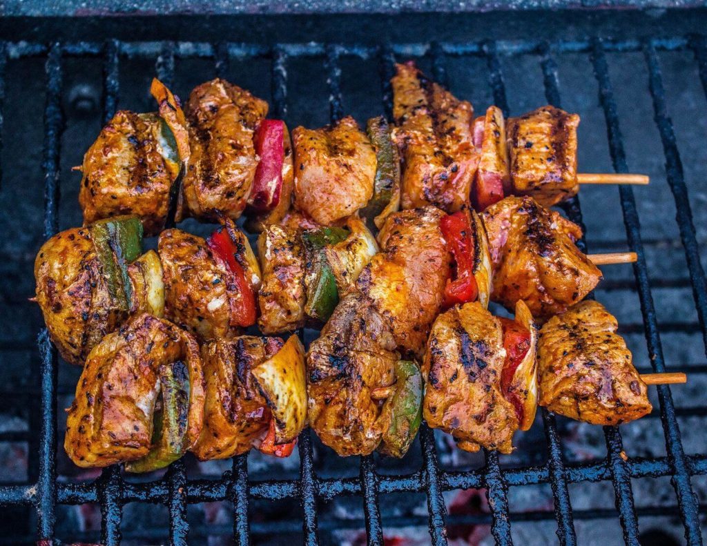 Grilled chicken and vegetable skewers cooking on a barbecue grill, showcasing Tanzanian cuisine.