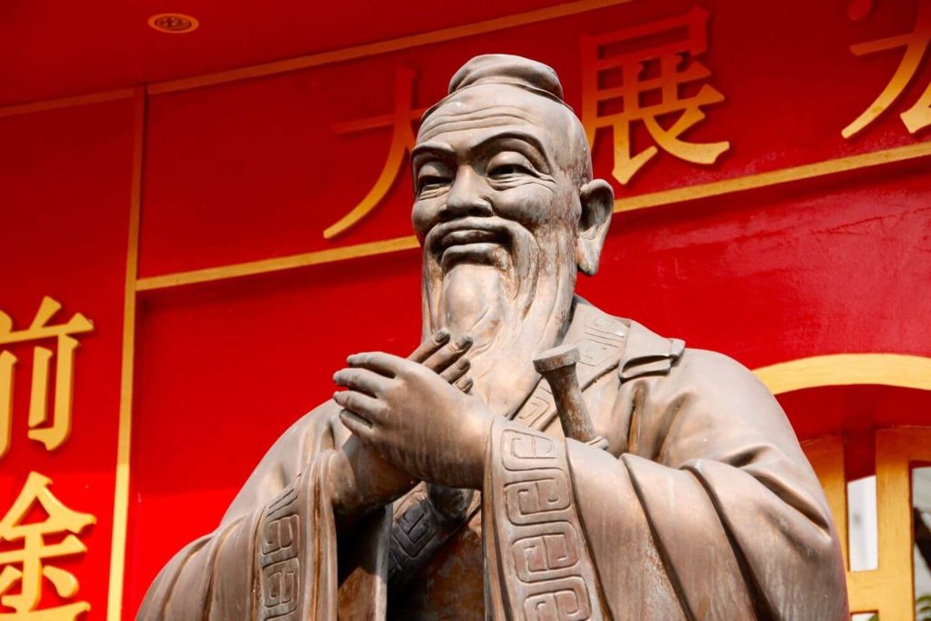 Bronze statue of a historical figure with a beard in front of a red background with Chinese characters, featured in your essential China travel guide.