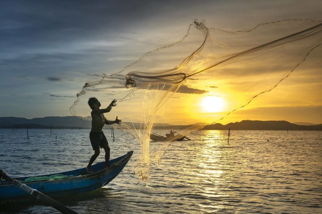 A fisherman casting a net from a boat at sunset, one of the best things to see in Vietnam.