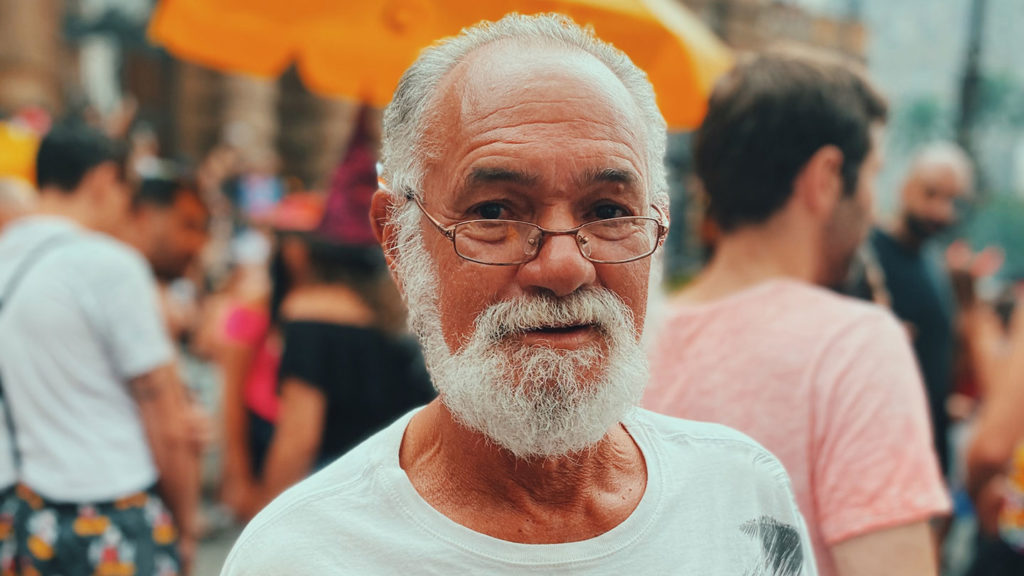 Elderly tourist man with a white beard looking at the camera at a crowded outdoor event in South America.