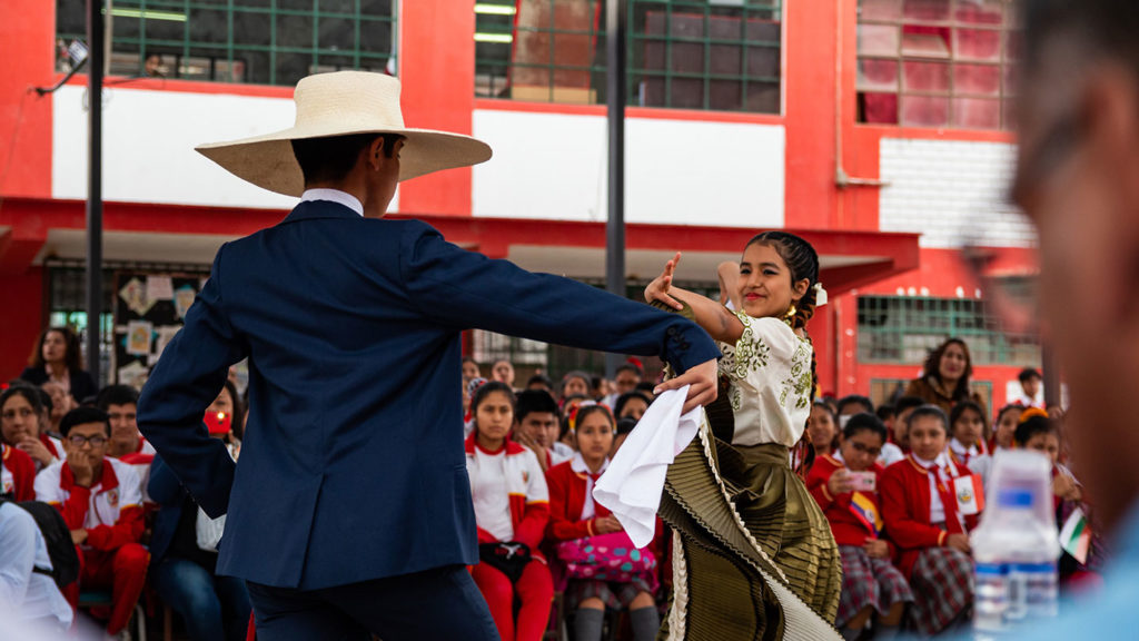 Traditional dance performance at a school event with an audience of students, faculty, and tourists in South America.