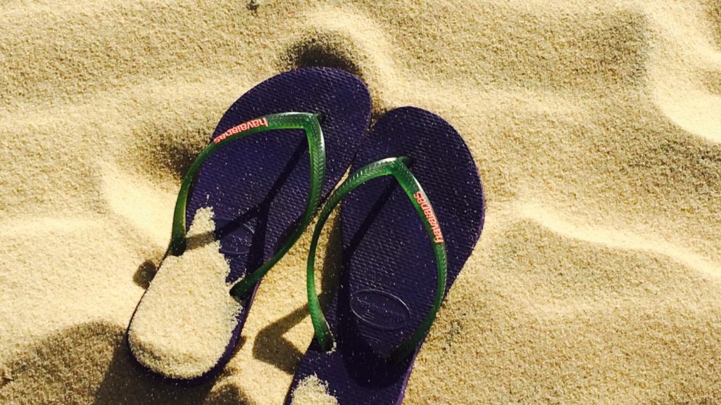A pair of navy blue flip-flops, reminiscent of the difference between Australia and New Zealand's flags, on sandy ground.