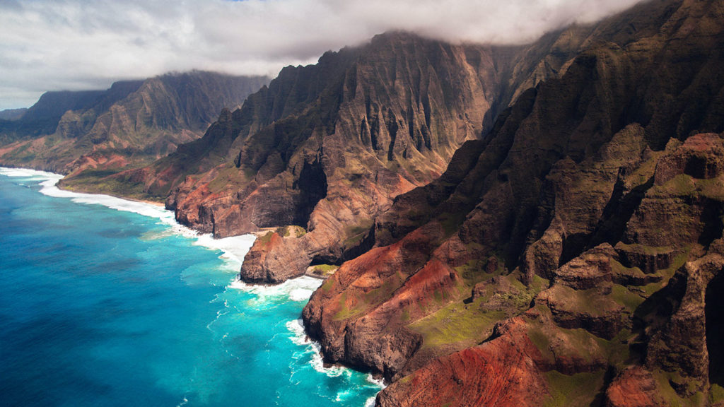 Aerial view of rugged coastal cliffs against turquoise ocean waters, a scene reminiscent of movies filmed in Hawaii.