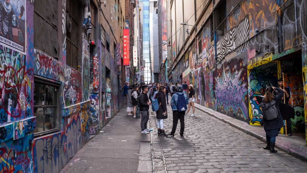 Tourists exploring a vibrant graffiti-covered alleyway on the east coast of Australia while a person takes a photograph.