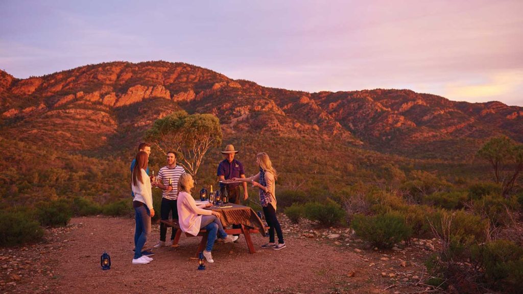 A group of friends enjoying an outdoor meal in the wilderness of Outback Australia at dusk.