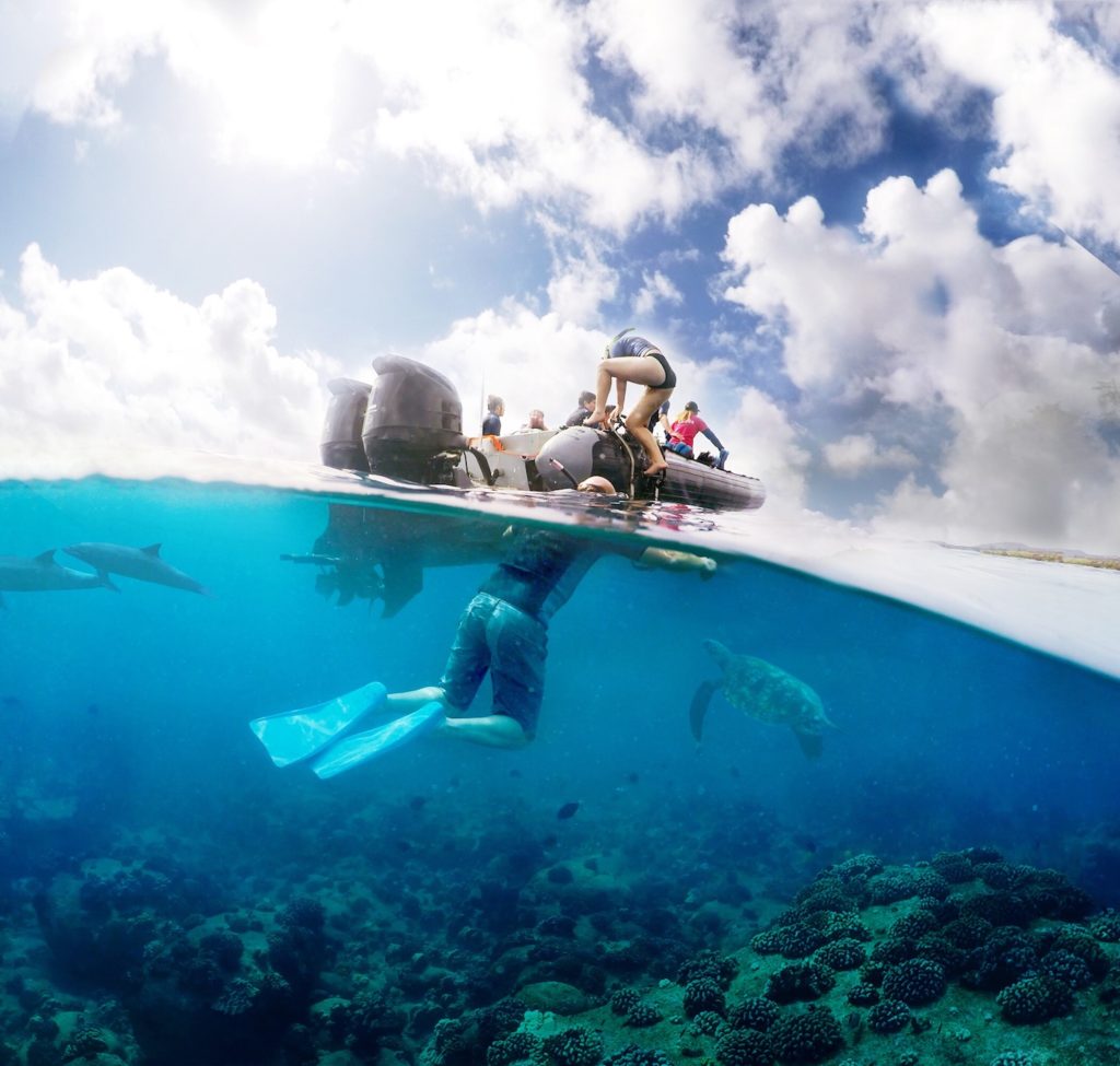 Snorkeler underwater observing marine life with nearby spectators on a boat during a Tour to Hawaii.