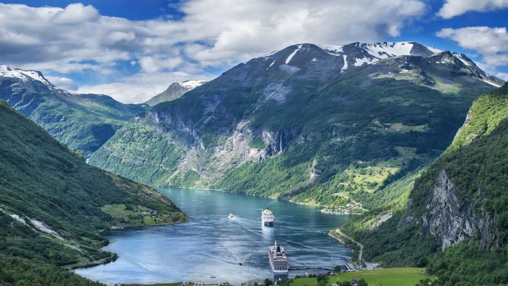 Cruise ships navigating through a majestic fjord surrounded by lush green slopes and rugged mountain peaks, a tour with Trafalgar reveals nature's wonders.