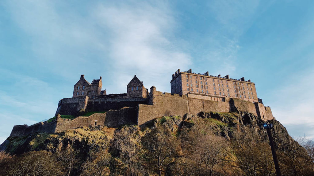 Edinburgh Castle, a highlight of Scotland travel experiences, sitting atop a rocky hill under a clear blue sky.