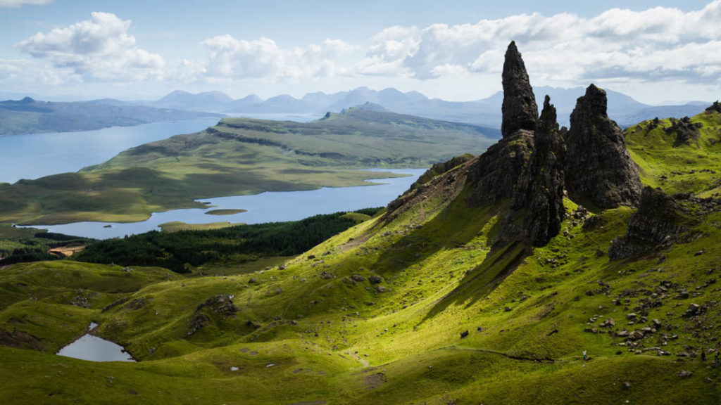 Verdant hills and rocky spires overlooking a serene loch in Scotland's rugged landscape offer unparalleled travel experiences.