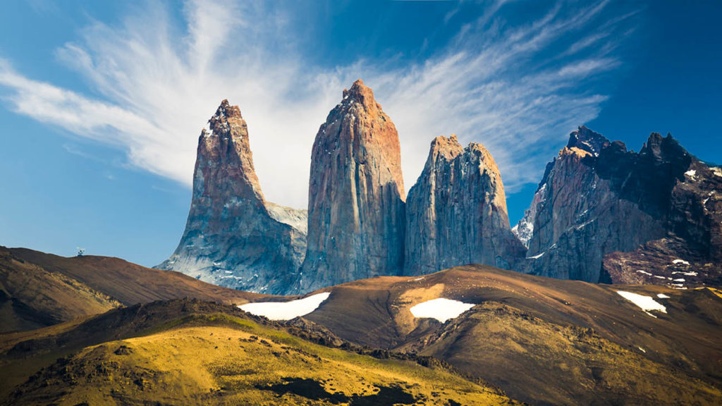 Rugged mountain peaks against a vivid blue sky with wisky clouds in the UNESCO-listed Patagonia, a bucket list destination for adventure seekers.