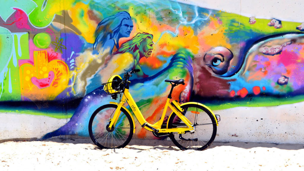 A yellow bike parked in front of a colorful graffiti wall in one of the best neighbourhoods in Sydney.