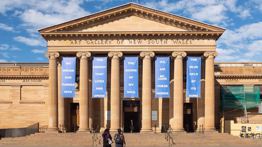 Visitors approaching the entrance of the art gallery of New South Wales under a clear blue sky, in one of the best neighbourhoods in Sydney.