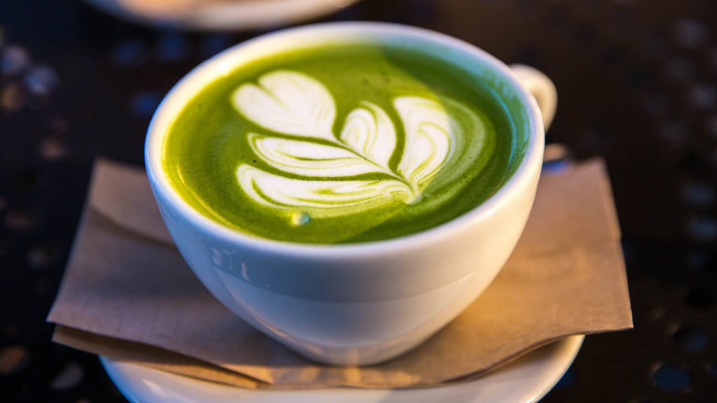 A cup of matcha latte with artful foam design on top, enjoyed in one of the best neighbourhoods in Sydney, placed on a saucer over a napkin.