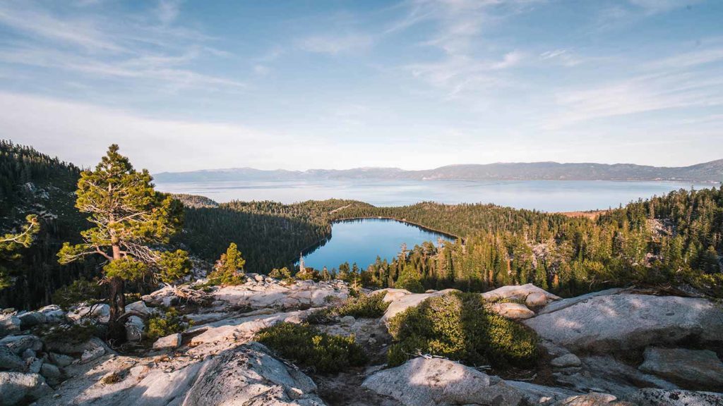 An expansive view of one of the most beautiful American lakes, a serene alpine lake surrounded by forested mountains under a clear sky.