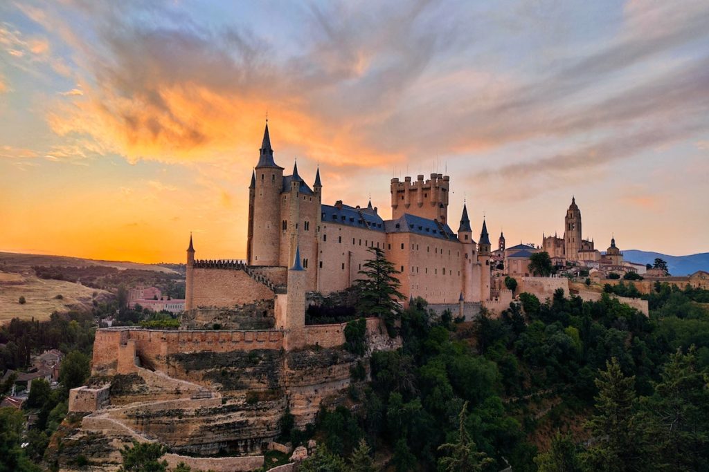 Historic castle bathed in the warm glow of sunset with dramatic clouds overhead, now accessible through quarantine-free travel.