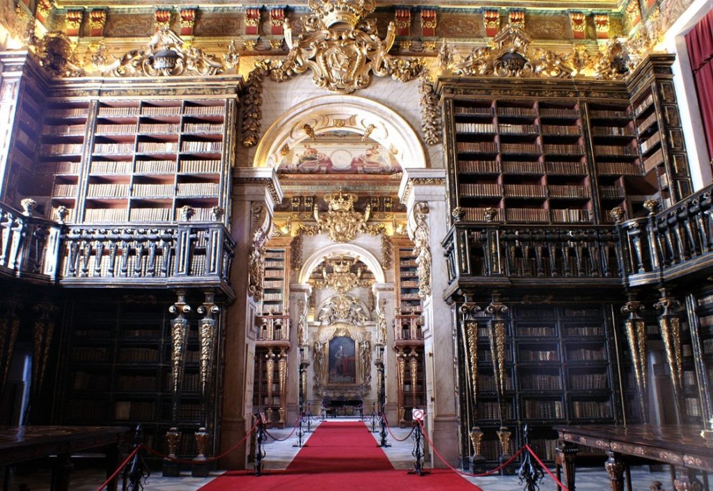 Grand and ornate historical library interior with wall-to-wall bookshelves, gilded arches, and a red carpet aisle, showcasing interesting facts about Portugal.